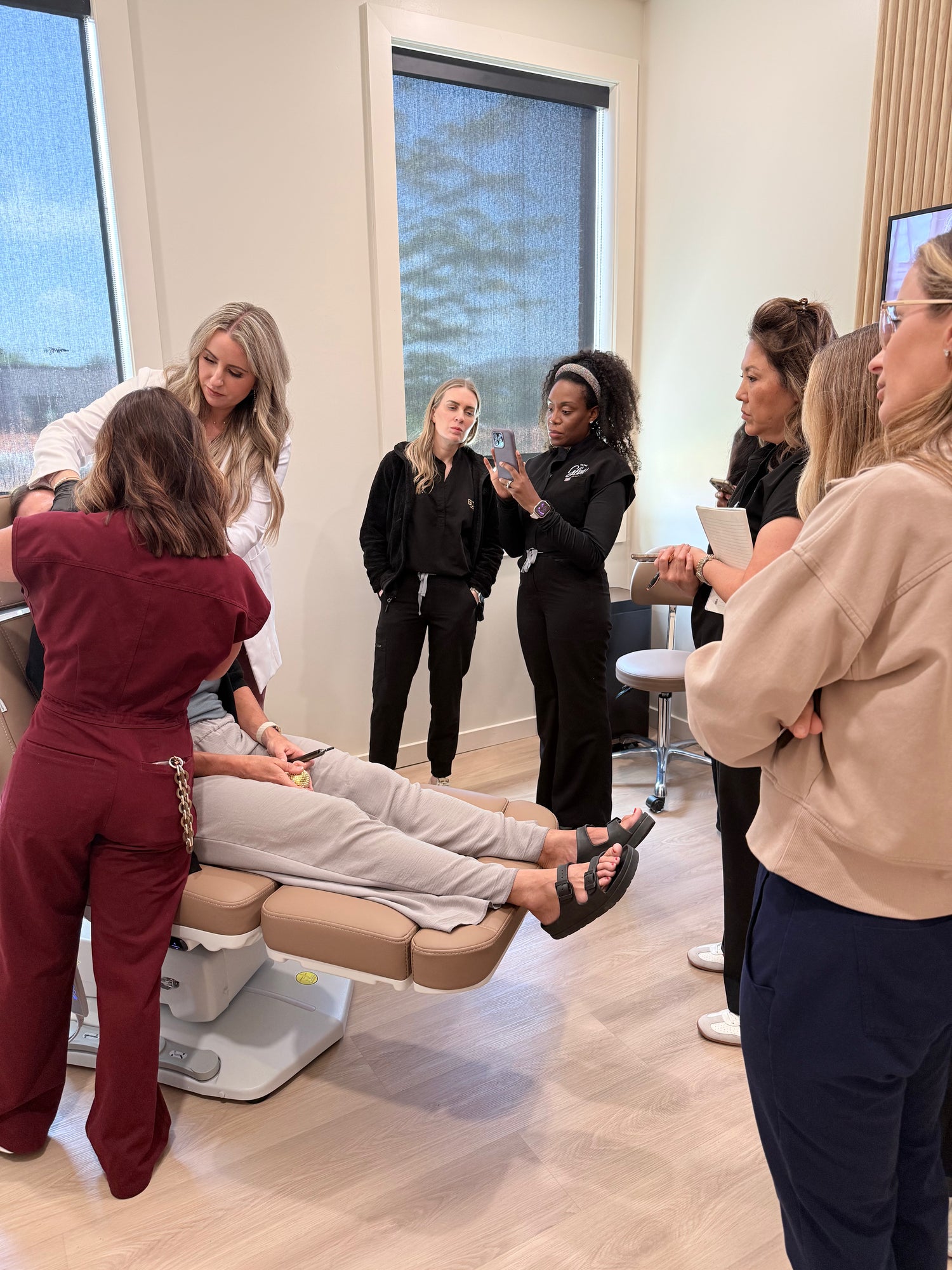 A group of women wearing scrubs standing around a woman in a clinical chair.